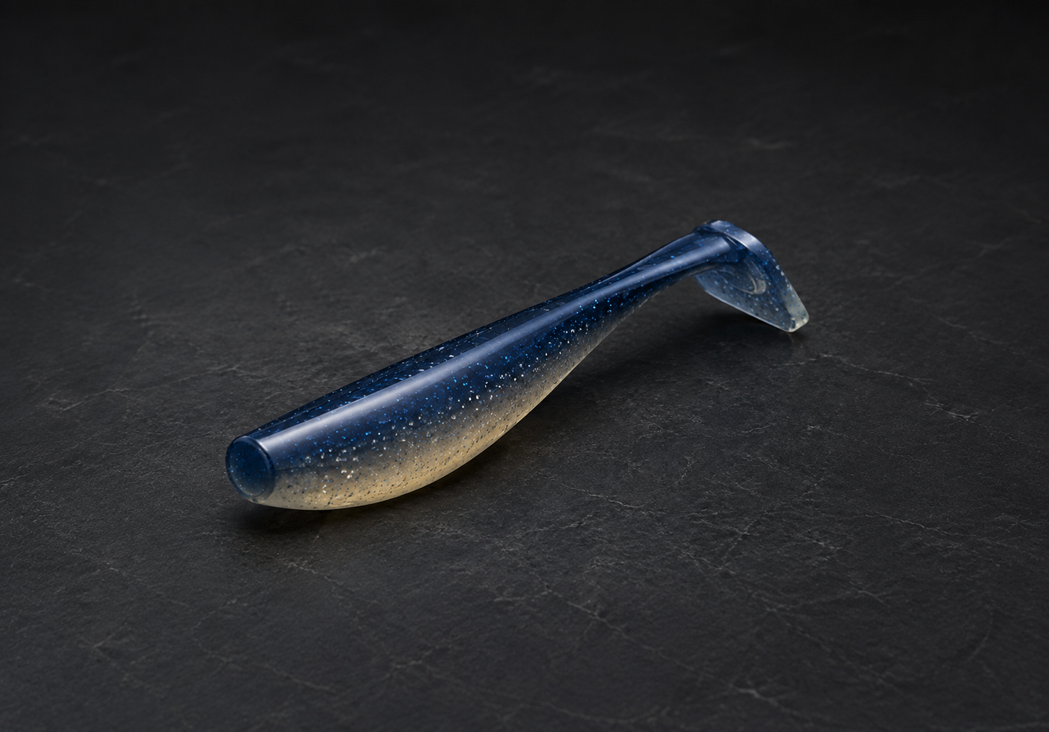 SaltVector 90mm paddletail soft plastic lure in blue and translucent finish on a dark textured surface