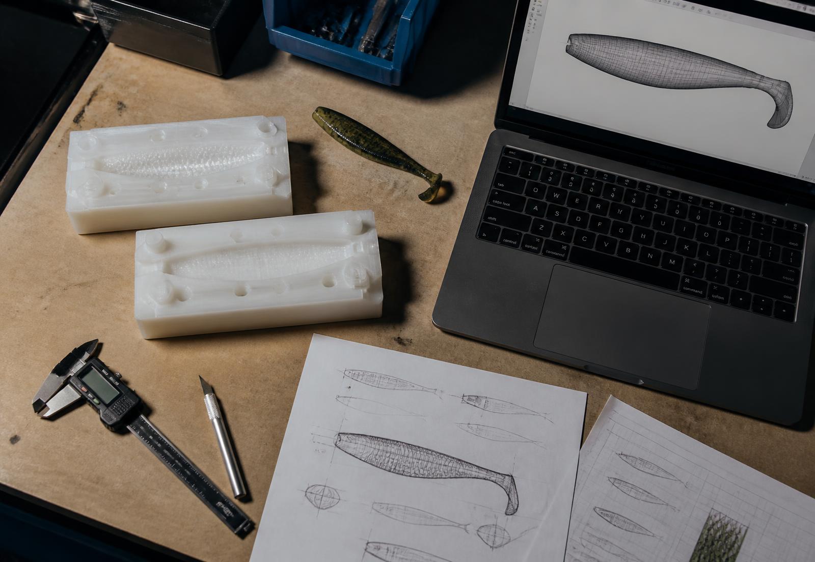 Prototype lure moulds, CAD model and design sketches on a workshop bench